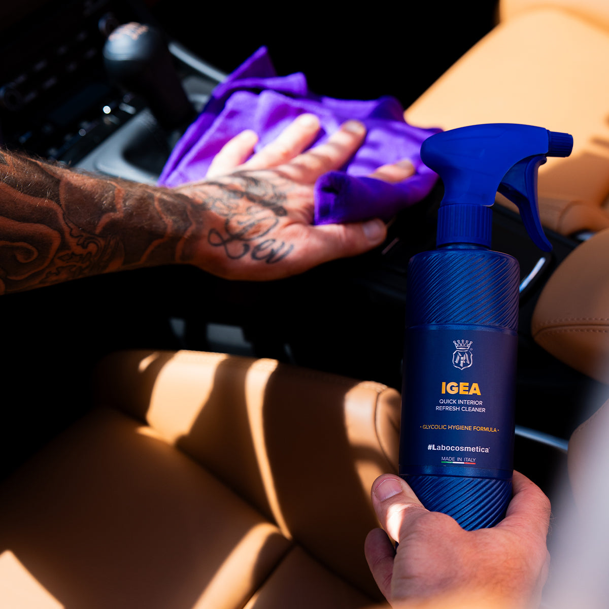 Person cleaning a car interior with a blue spray bottle labeled 'IGEA' and a purple cloth.