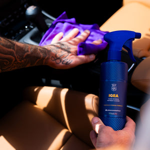 Person cleaning a car interior with a blue spray bottle labeled 'IGEA' and a purple cloth.
