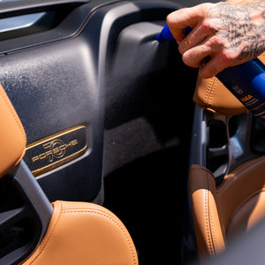 Person cleaning a Porsche car interior with a spray bottle.