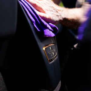 Person cleaning a Porsche car interior with a purple microfibre towel.