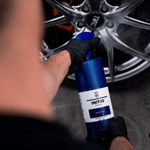 Person holding a bottle labeled 'INITIO' near a car wheel