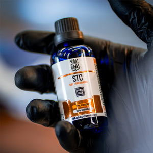 Bottle of STC product held by a gloved hand against a blurred background