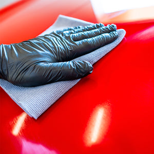 Hand wearing a blue glove cleaning a red surface with a cloth