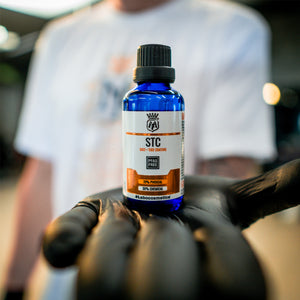 Bottle of STC product held by a person wearing black gloves with a blurred background