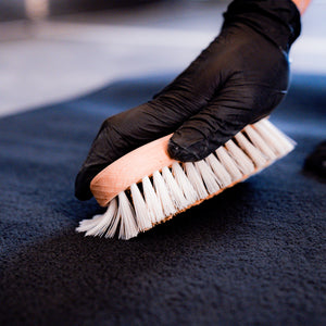 Hand wearing a black glove holding a brush on a dark surface