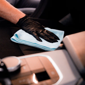 Person cleaning car interior with a microfiber cloth and black gloves