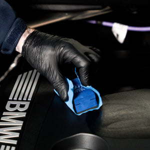 Person cleaning a BMW car interior with a blue microfiber cloth.