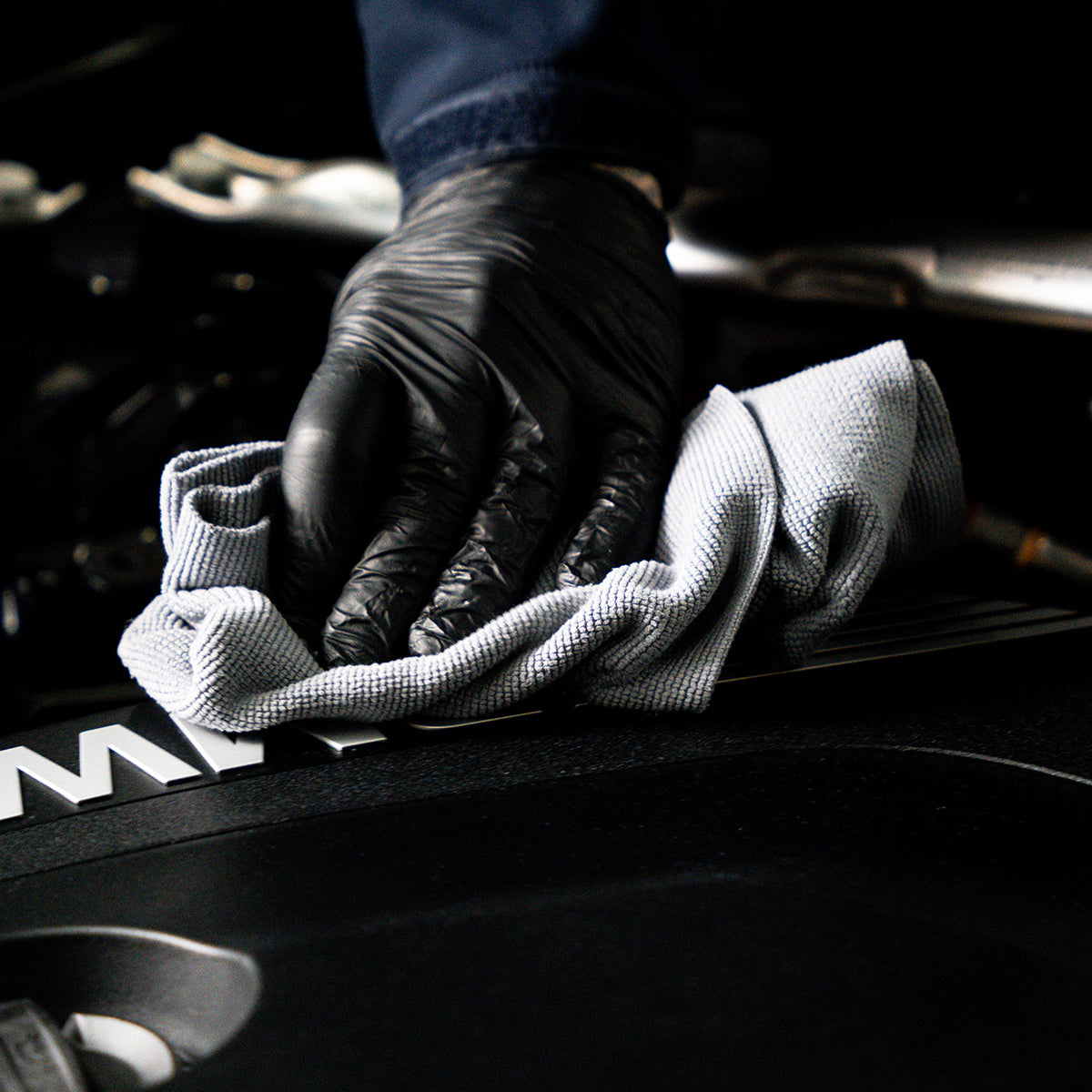 Person cleaning a car engine with a white cloth, wearing black gloves.