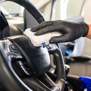 Person cleaning a car's steering wheel with a cloth and black gloves.