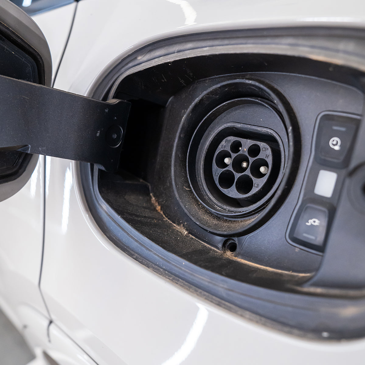 Electric vehicle charging port with a plug inserted on a white car.