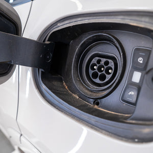 Electric vehicle charging port with a plug inserted on a white car.