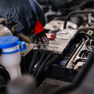 Person wearing black gloves using a red tool on a car engine