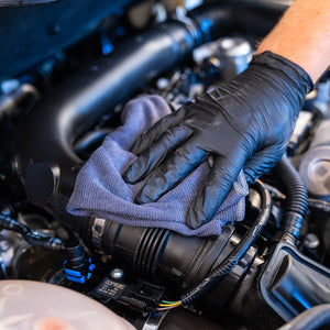 Person wearing black gloves cleaning engine components with a blue cloth