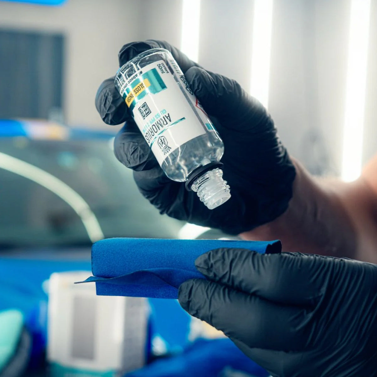 Bottle of Armorius PPF Coating Gloss held by a hand with a blue car in the background