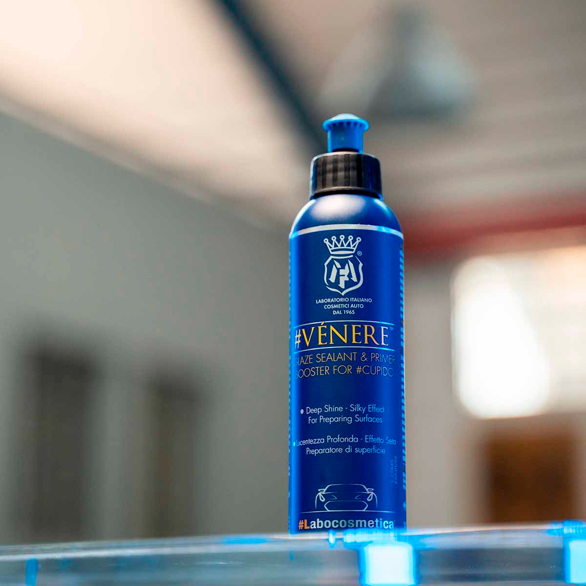 Blue bottle of 'VENERE' product on a reflective surface with a blurred background