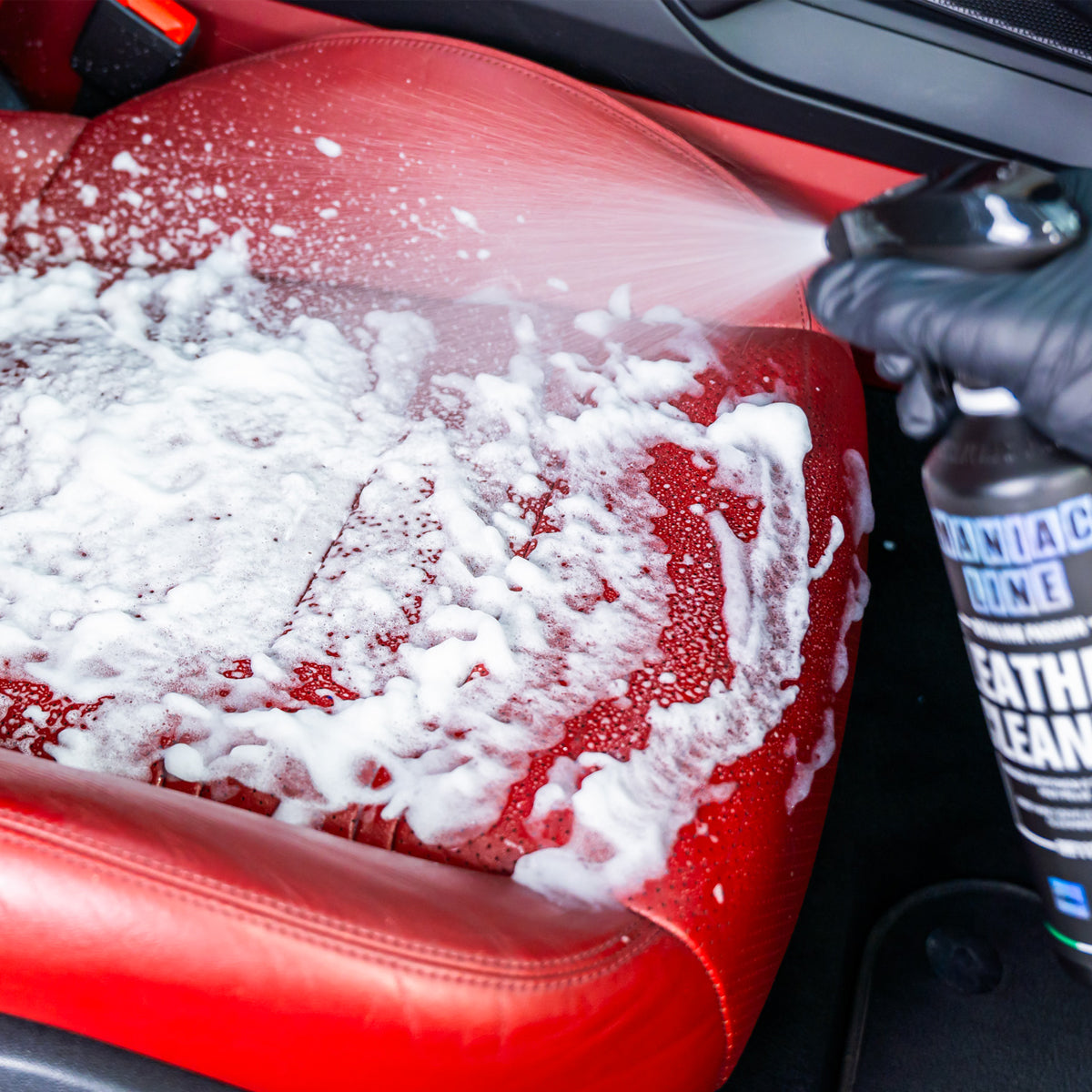 Red car seat being cleaned with a bottle of leather cleaner.