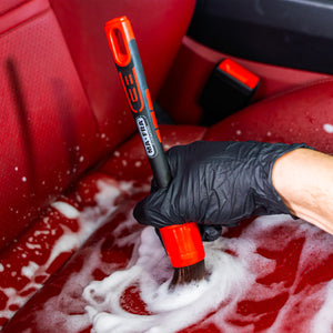 Person cleaning a red car seat with a brush and soapy water