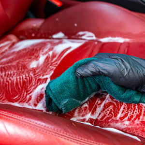 Person cleaning a red car seat with a green cloth