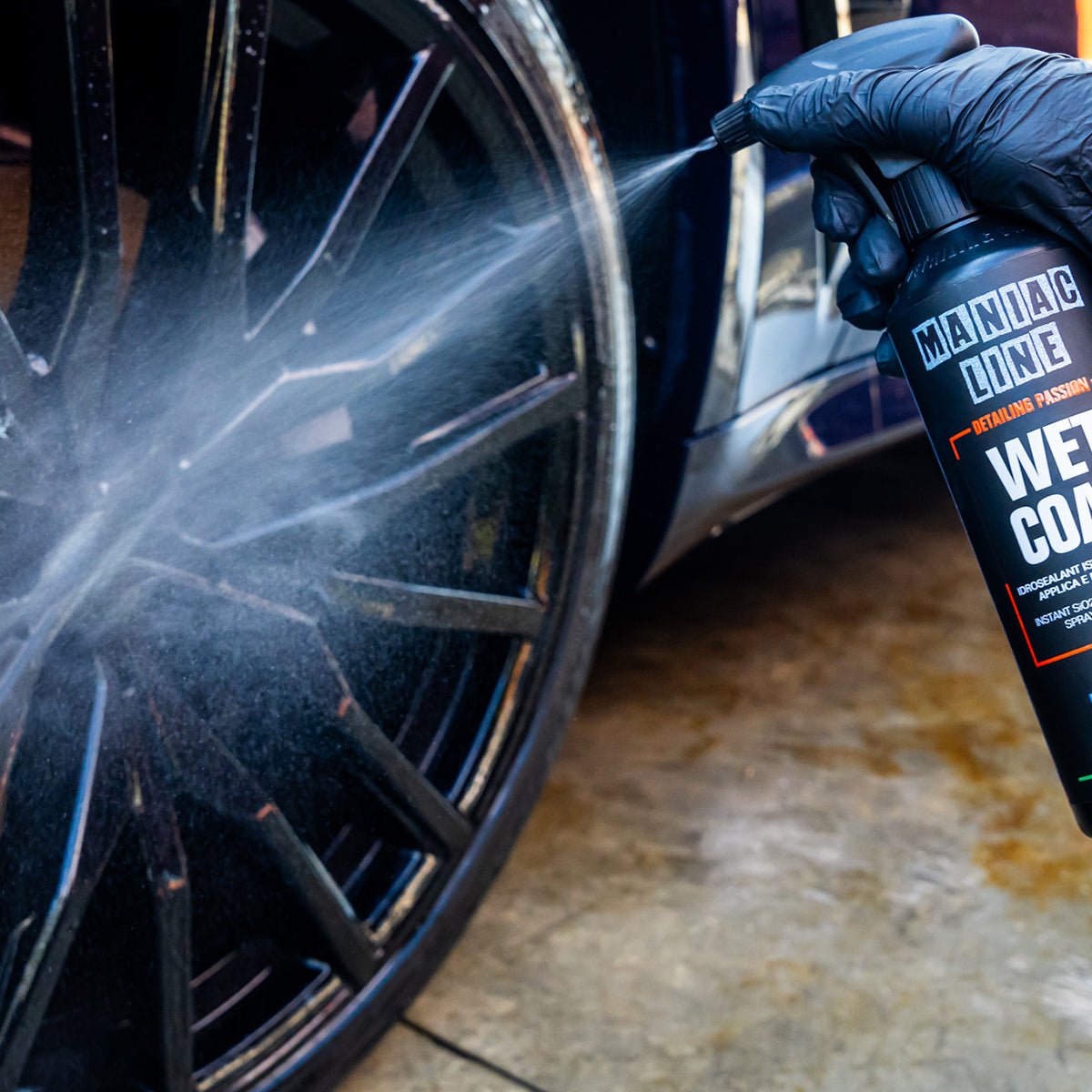 Person cleaning a car wheel with a spray bottle labeled 'Maniac Line Wet Coat'.