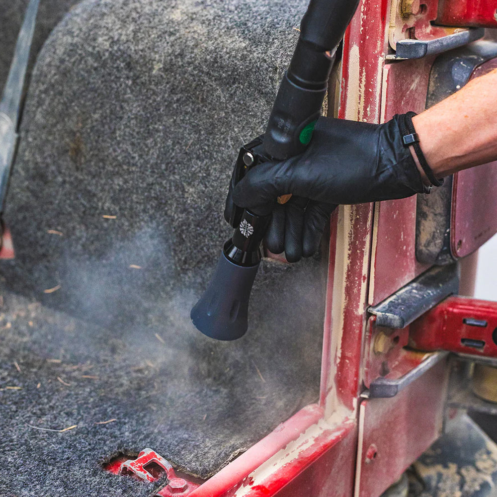 Person using a pressure tool to clean a red vehicle door with a black spray gun.