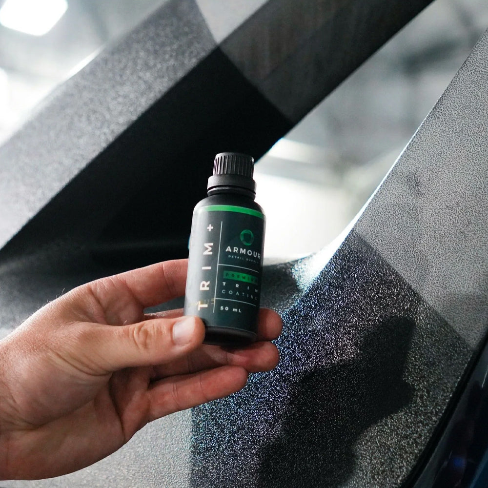 Hand holding a small bottle labeled 'ARMOUR' against a car interior background