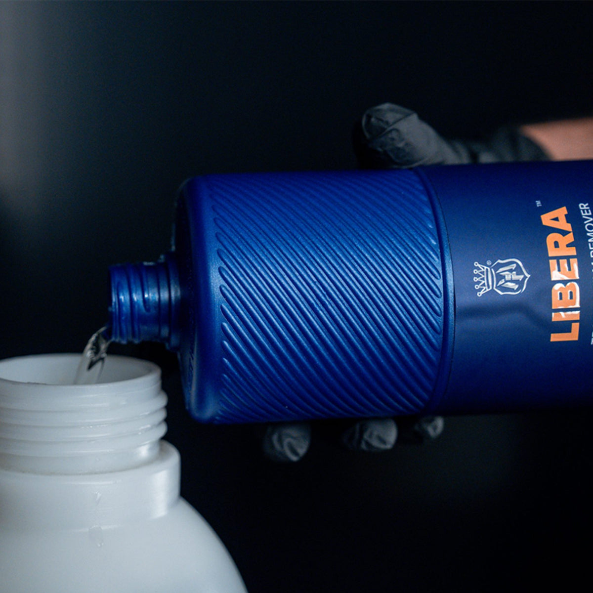 Blue Libera bottle being poured into a white container against a dark background