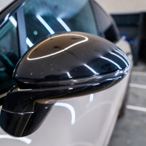 Close-up of a car's black side mirror on a white car.