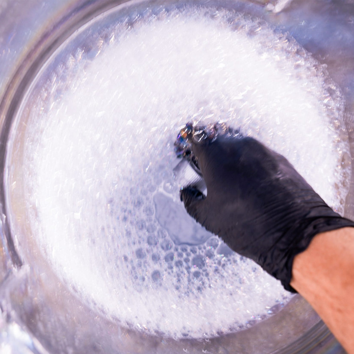 Hand wearing a black glove cleaning something in a bowl filled with soapy water.