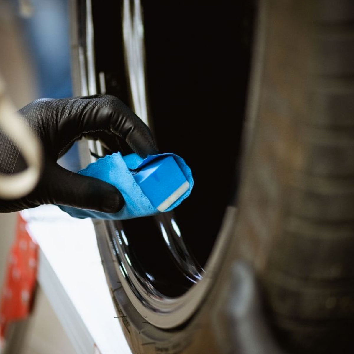 Person cleaning a car tire with a blue sponge and black glove.
