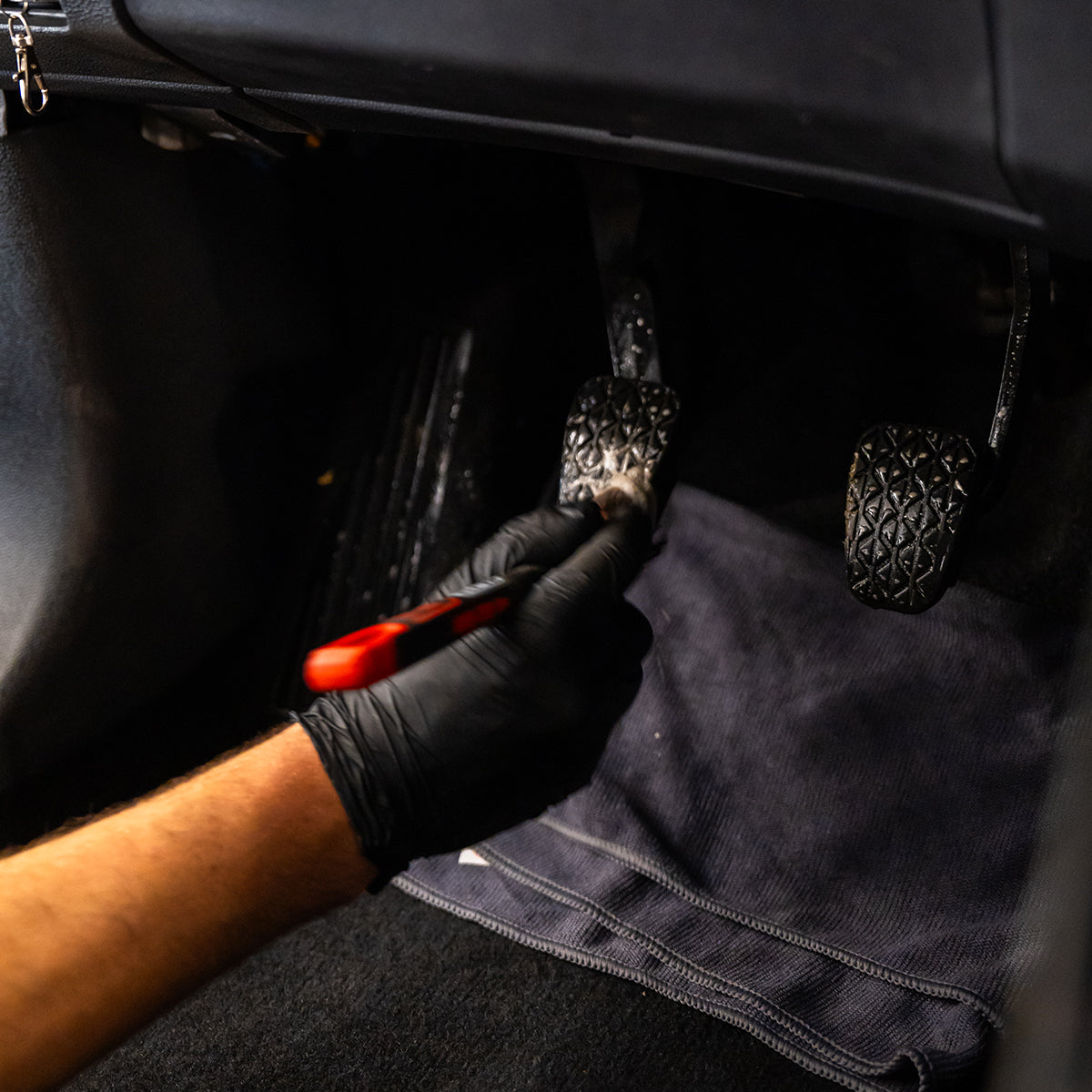 Person wearing black gloves using a tool on car interior components.