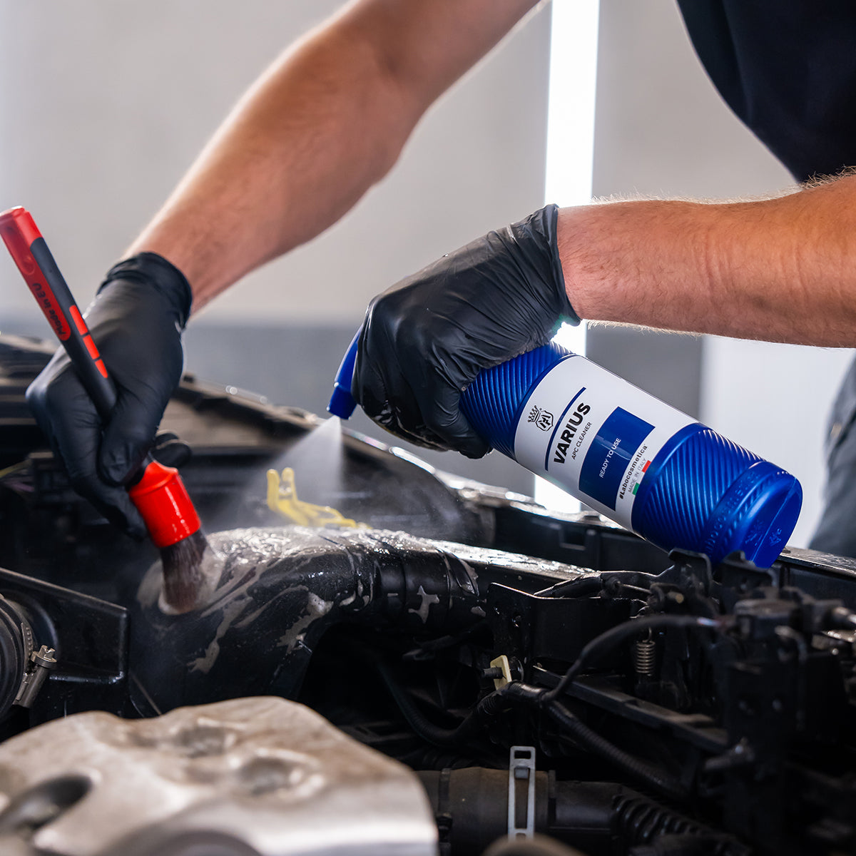 Person working on a car engine with a bottle of VARIS lubricant and a brush.
