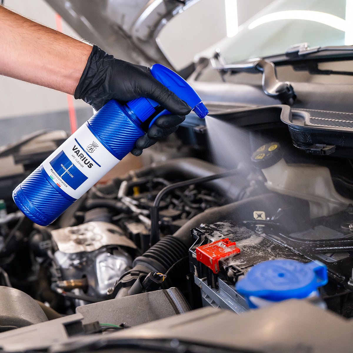 Person using a blue spray can labeled 'Varius' on a car engine.