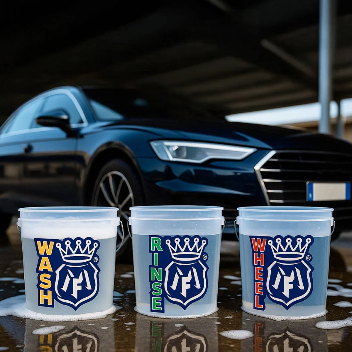 Three labeled buckets for car washing with a car in the background.