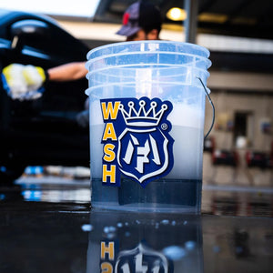 Clear bucket with 'WASH' logo held by a person at a car wash with Audi cars in the background.