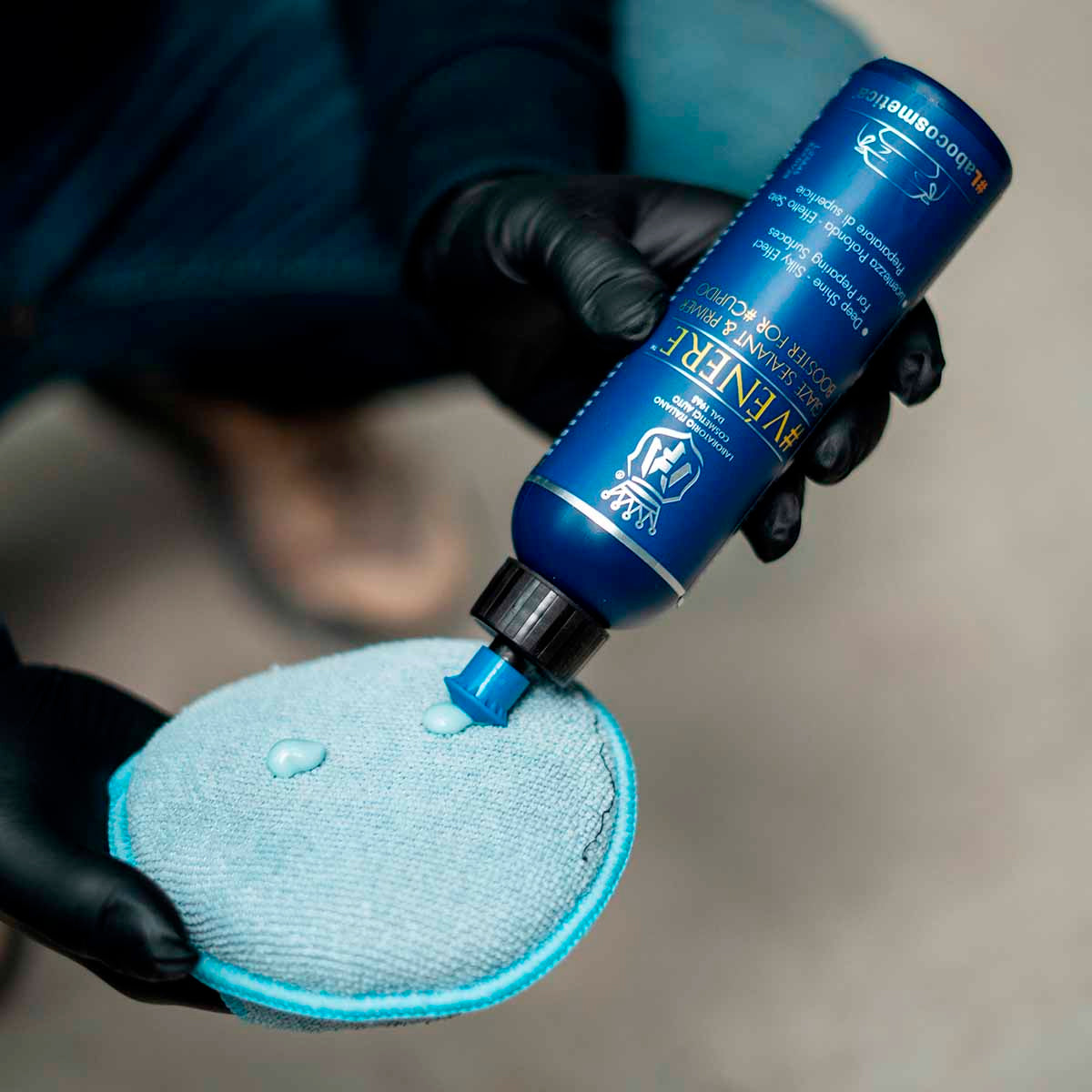 Person applying a blue bottle of car care product to a blue microfiber pad.
