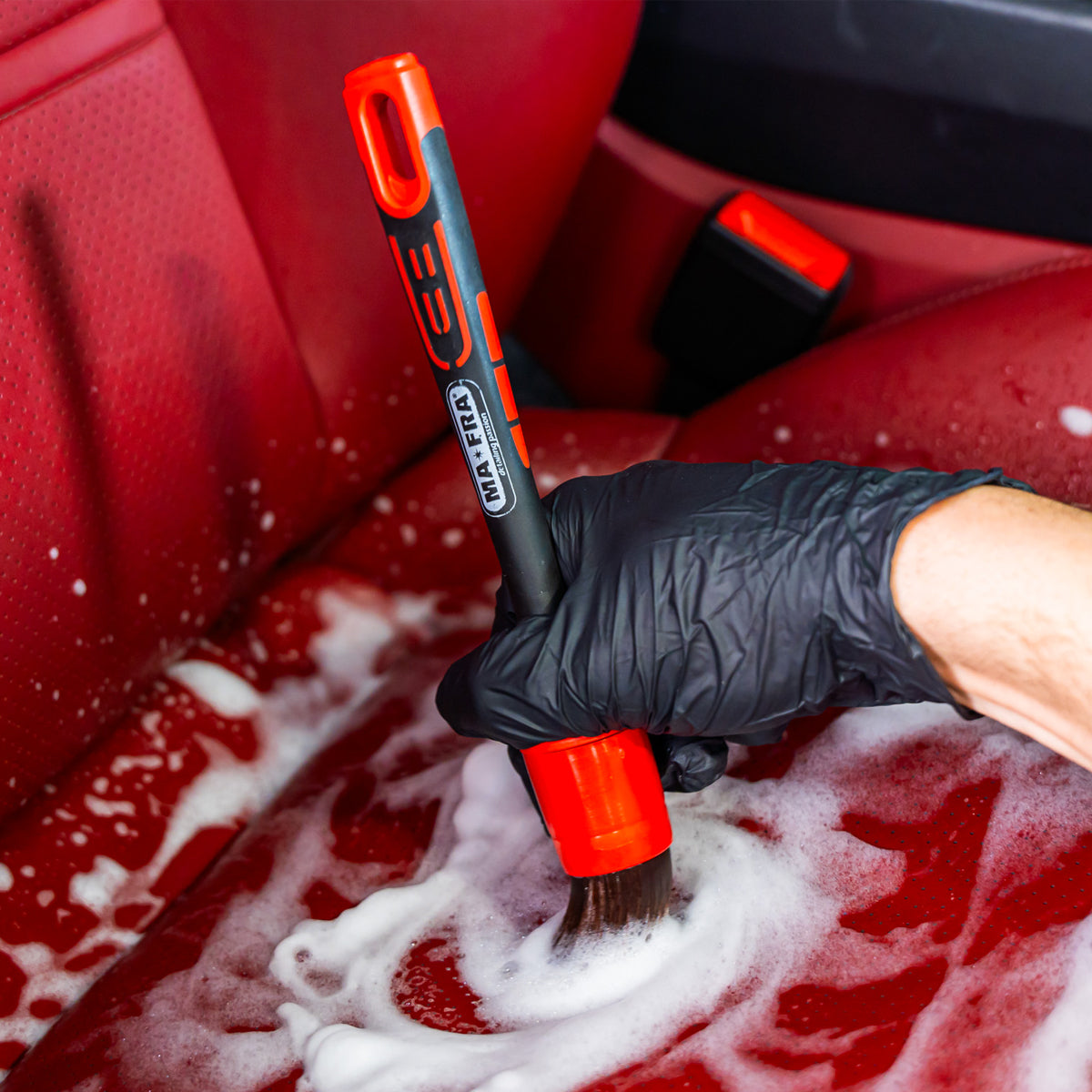 Person cleaning a red car seat with a brush and soapy water