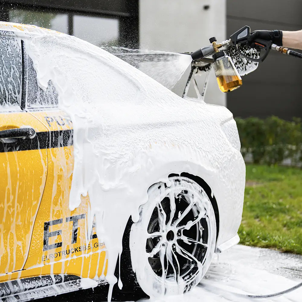 Car being washed with a high-pressure water gun, covered in soap suds.