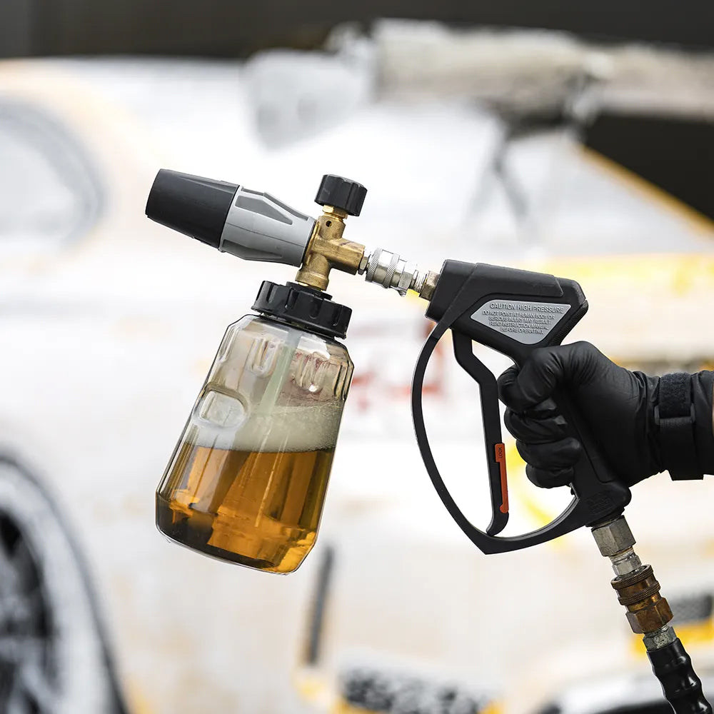 Foam cannon for car washing held by a gloved hand with a blurred car in the background